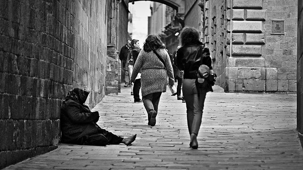 Poor elderly women sitting on a street as people walk by