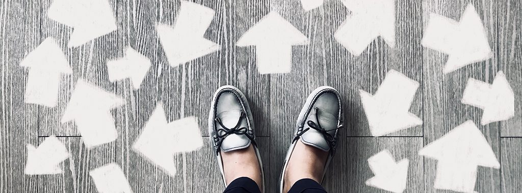 A view of shoes standing on a road painted with arrows pointing in different directions.