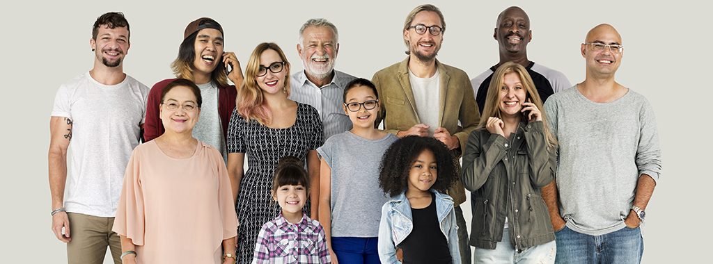 A diverse group of smiling adults and children. Some of whom are talking on cell phones.