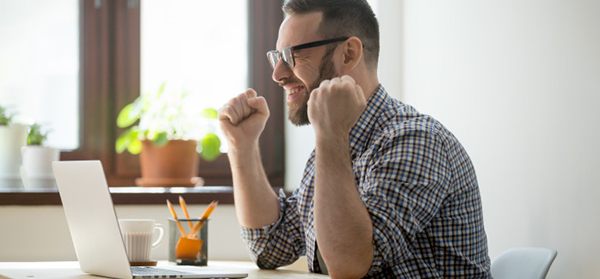 successful businessman celebrating his victory raising arms, in front of a laptop