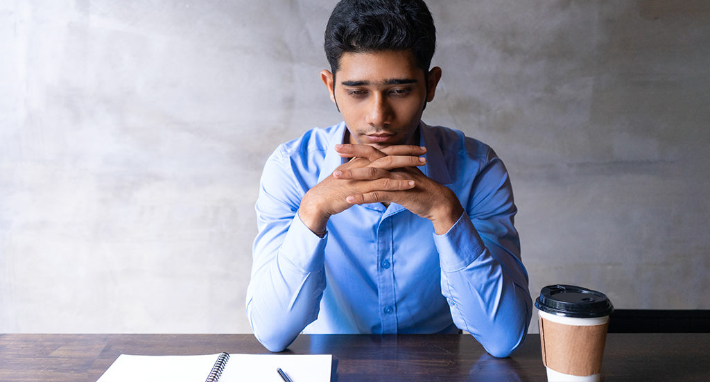 Sad man thinking while seated at a table with a pad of paper and cup of coffee