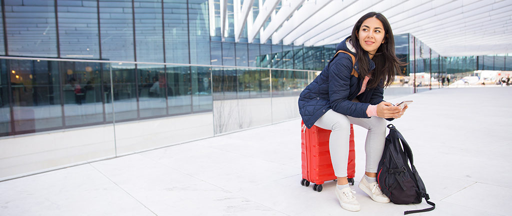 Positive young woman at an airport surfing on smartphone